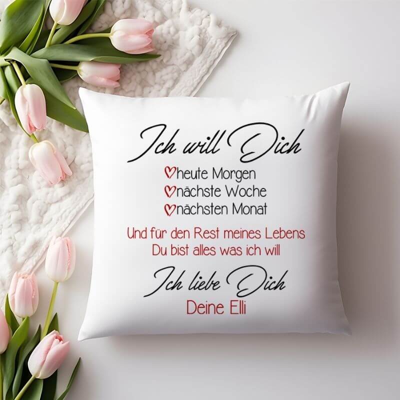 Weißes Kissen mit romantischem Spruch „Ich will Dich – heute Morgen, nächste Woche, nächsten Monat“ auf weicher Decke, dekoriert mit zartrosa Tulpen.