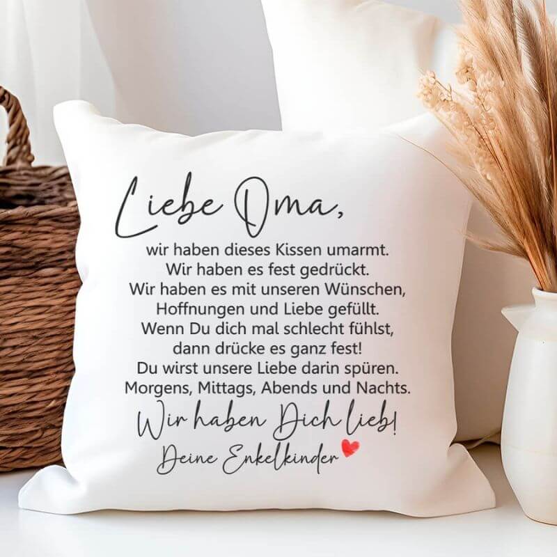 Flauschiges Kissen „Liebe Oma – Kissen umarmt“ in der Wir-Form, an einem Korb mit Deko-Pflanzen platziert.