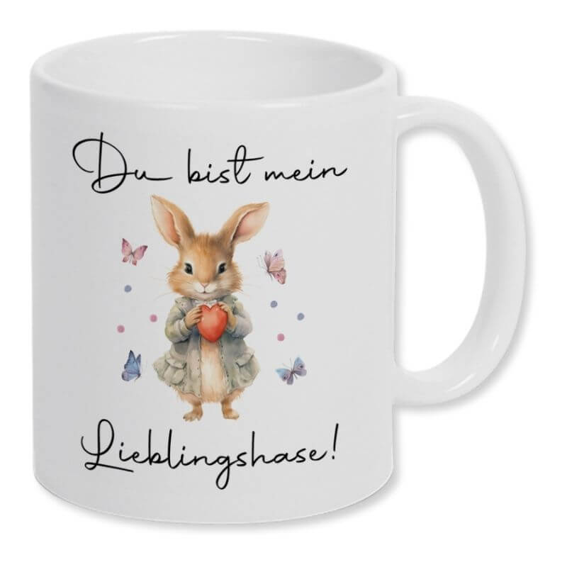 Weiße Keramiktasse mit dem Schriftzug "Du bist mein Lieblingshase". Mittig ist ein süßer Hase mit einem Herz in den Händen zu sehen. Um ihn herum fliegen vier Schmetterlinge.
