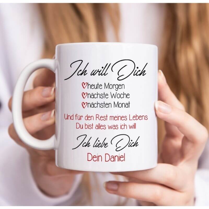 Frau hält weiße Tasse mit der romantischen Aufschrift "Ich will Dich – heute Morgen, nächste Woche, nächsten Monat – Ich liebe Dich, Dein Daniel" in den Händen.