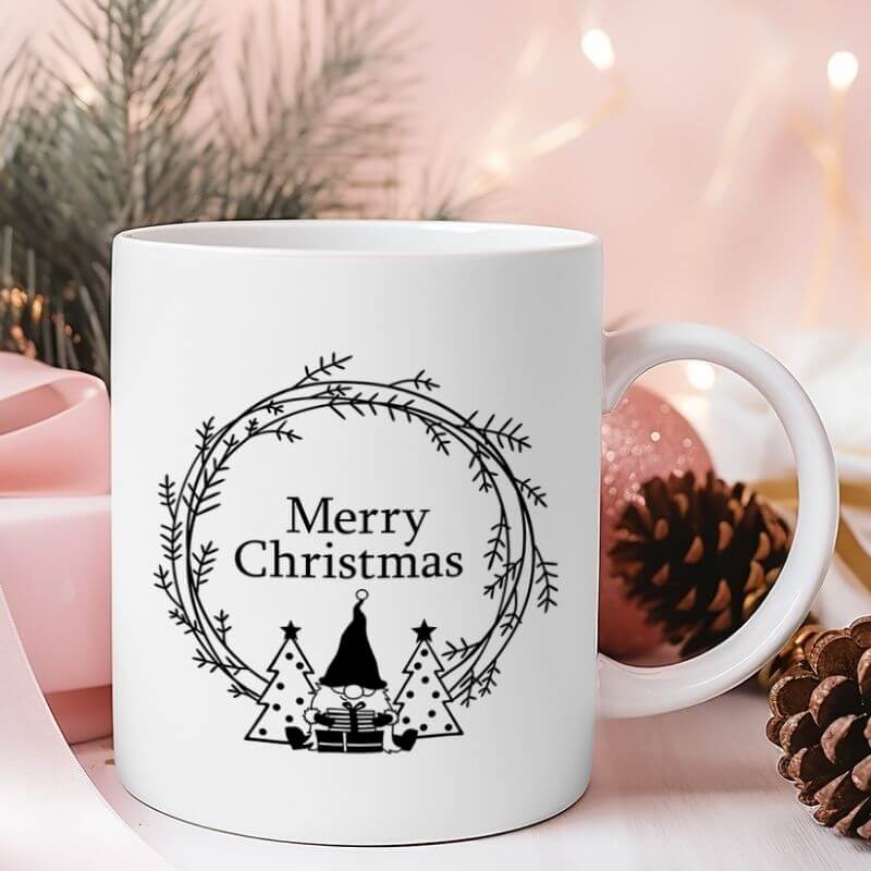 Weiße Weihnachtstasse mit Gnome-Design und Aufschrift "Merry Christmas", liebevoll platziert zwischen Tannenzapfen, Lichterkette und rosa Weihnachtskugel.