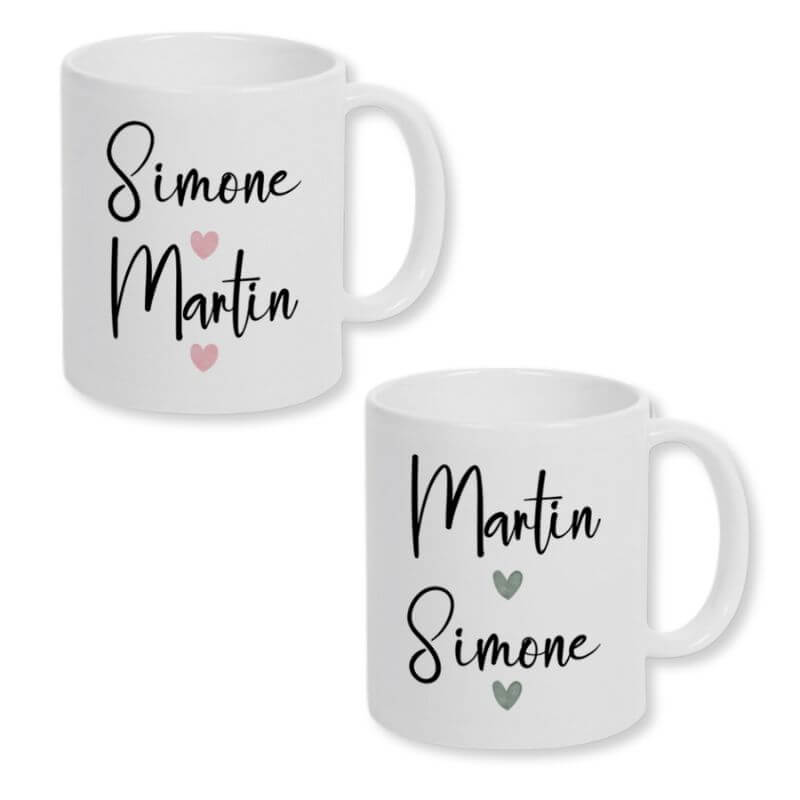 Partnertassen mit Wunschnamen. Zwei weiße Keramiktasse mit einem Print mit den Namen des Paares und zwei Herzen im Watercolor-Design. Für die Frau mit rosafarbenen Herzen und für den Mann mit grauen Herzen. Der Print befindet sich auf beiden Seiten der Tassen.