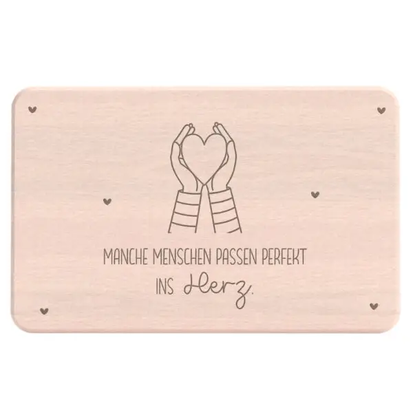 Frühstücksbrettchen aus hellem Holz mit Gravur von zwei Händen, die ein Herz formen, darunter der Schriftzug „Manche Menschen passen perfekt ins Herz"